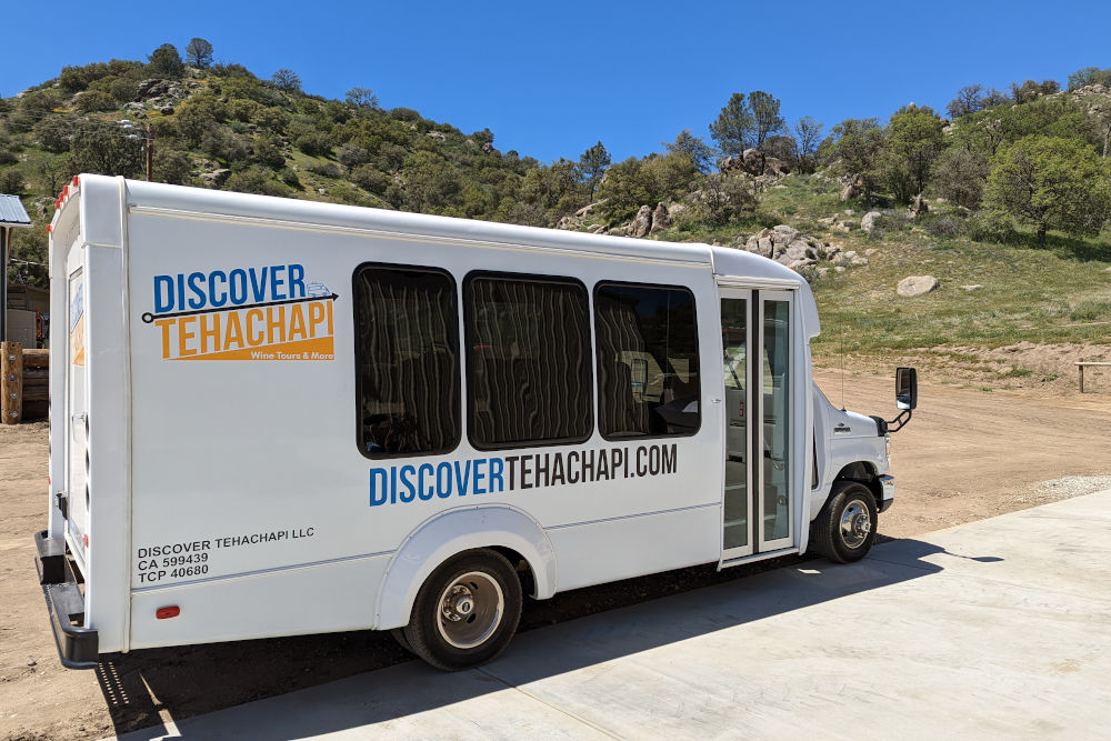 Discover Tehachapi bus with Tehachapi hills in spring bloom behind.